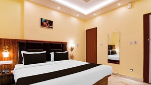 A hotel room with a large bed, a wooden headboard, a nightstand with a lamp, a wall-mounted mirror, and a painting. - Townhouse Puri Sea Beach (Puri)