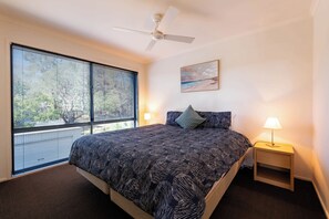 A bedroom with a bed, a ceiling fan, a painting, and a nightstand with a lamp. - She Oak Treetop Escape (Fairhaven)