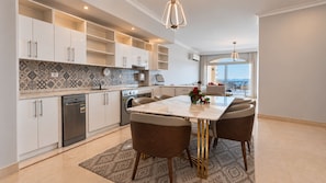A modern kitchen with white cabinets, a built-in oven, and a dining area with a marble table and brown chairs.