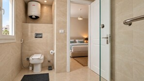A bathroom with a toilet, shower, and a glass door leading to a bedroom.