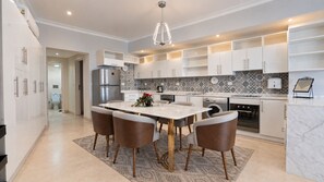 A modern kitchen with white cabinetry, a marble island, and a dining area with four chairs.