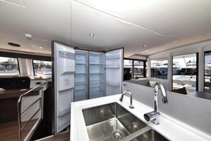 Cozinha moderna com pia de aço inoxidável, geladeira e janela com vista para um porto de iates.