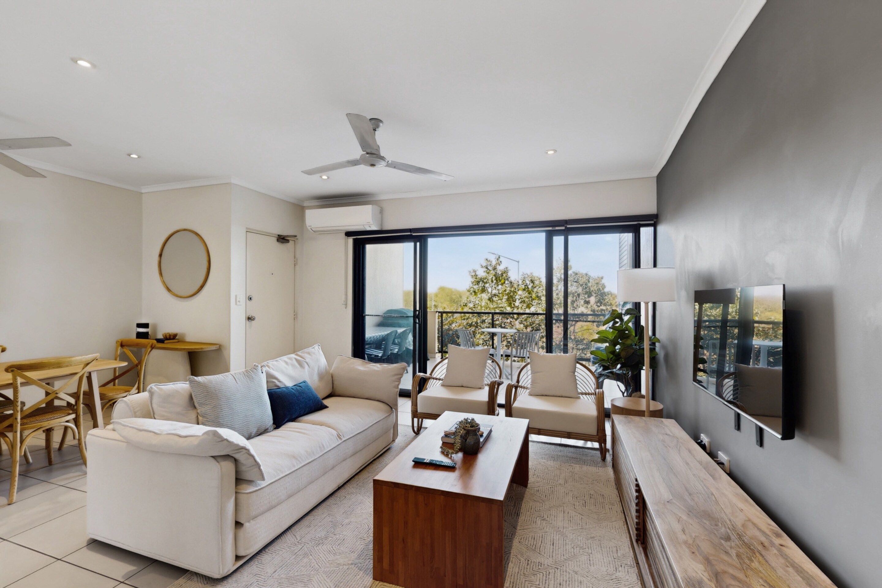 A modern living room with a sofa, coffee table, and chairs, a dining area with a table and chairs, and a large window with a view.