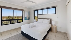 Ein Schlafzimmer mit einem großen Bett, einem Deckenventilator und Blick ins Freie durch ein großes Fenster.