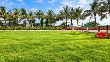 A well-maintained grassy lawn with a seating area featuring tables and chairs, surrounded by palm trees and a clear sky.