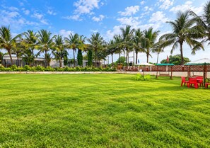 A well-maintained grassy lawn with a seating area featuring tables and chairs, surrounded by palm trees and a clear sky.