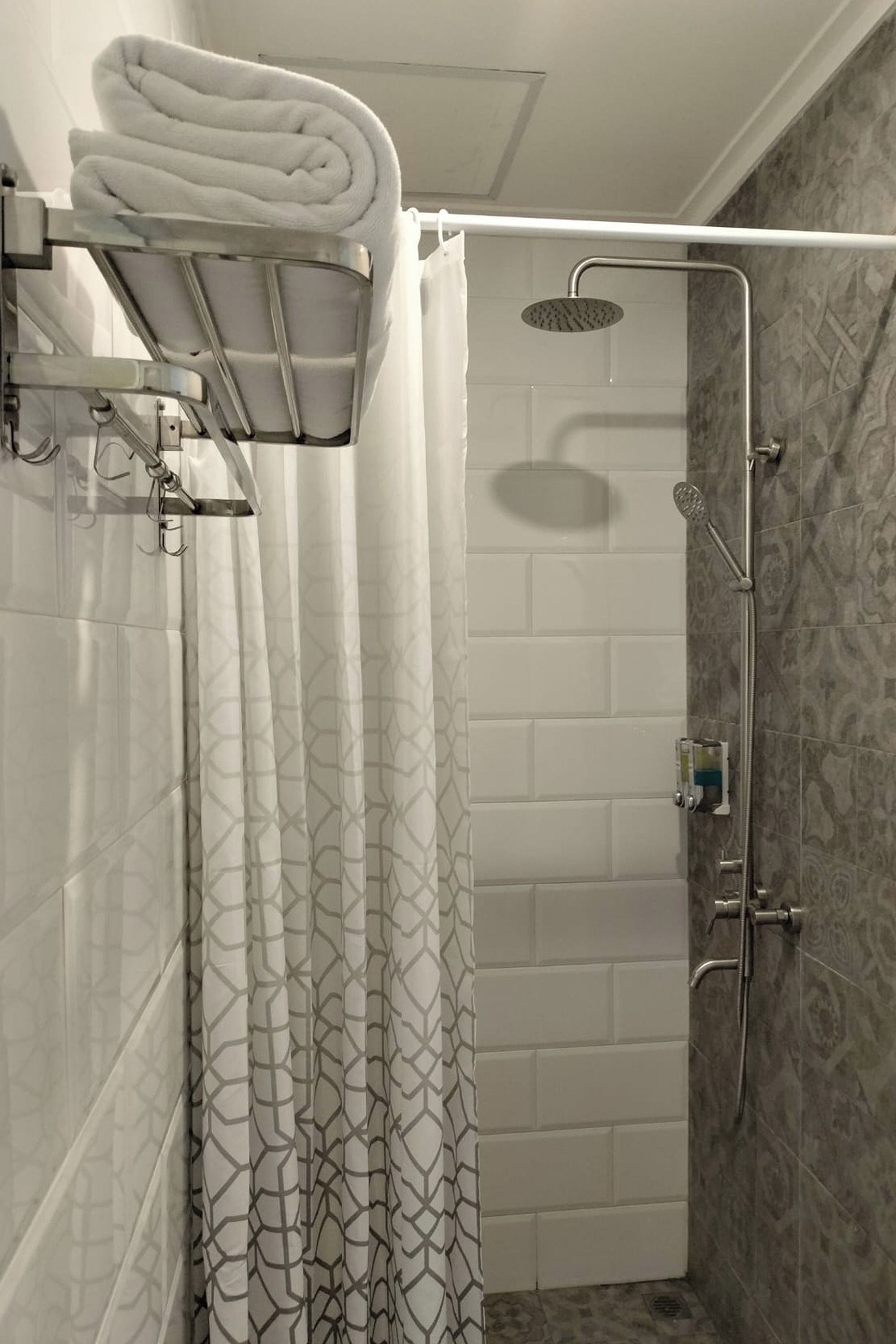 Une douche équipée d’un pommeau de douche à main, d’un porte-serviettes mural et d’un rideau de douche à motifs géométriques.