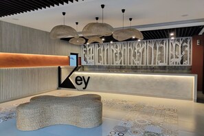 Zona de recepción con diseño moderno, que incluye un mostrador con la palabra 'ey' a la vista, un banco tejido y una pared decorativa con siluetas de árboles.