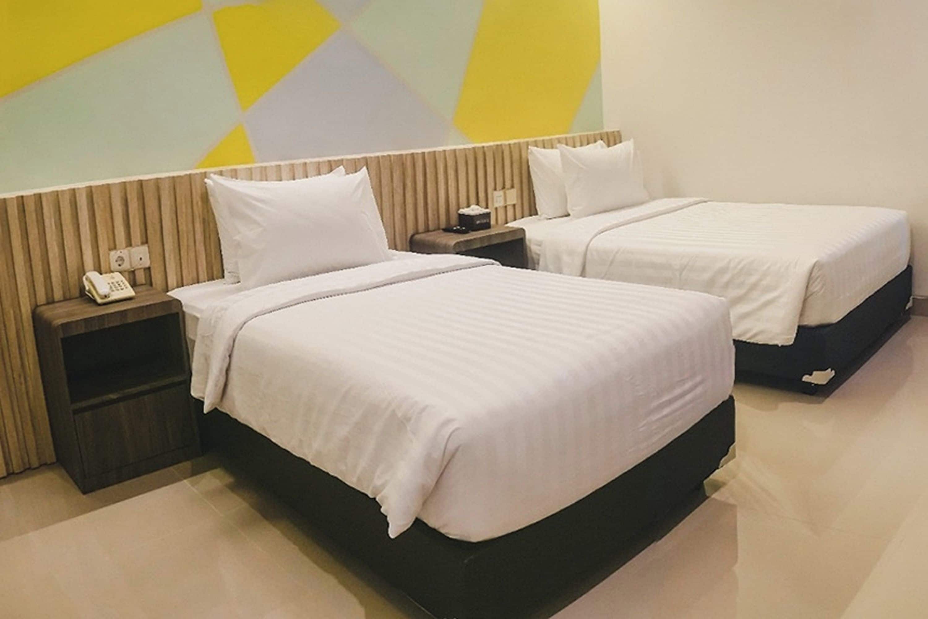 Une chambre d’hôtel avec deux lits, une table de chevet avec un téléphone et un mur orné d’un motif géométrique.