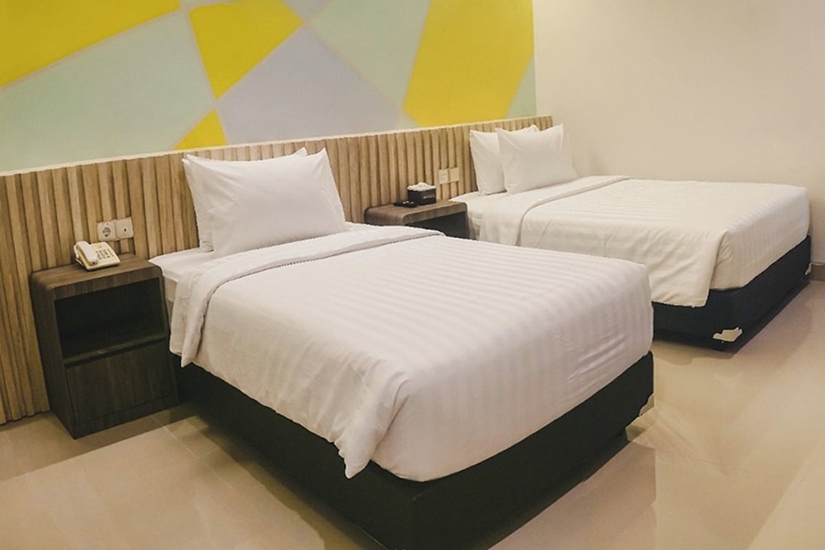 Habitación de hotel con dos camas, una mesita de noche con teléfono y una pared con diseño geométrico.