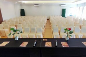 Un salón de conferencias con filas de sillas blancas y una mesa negra con micrófonos y tarjetas de identificación.