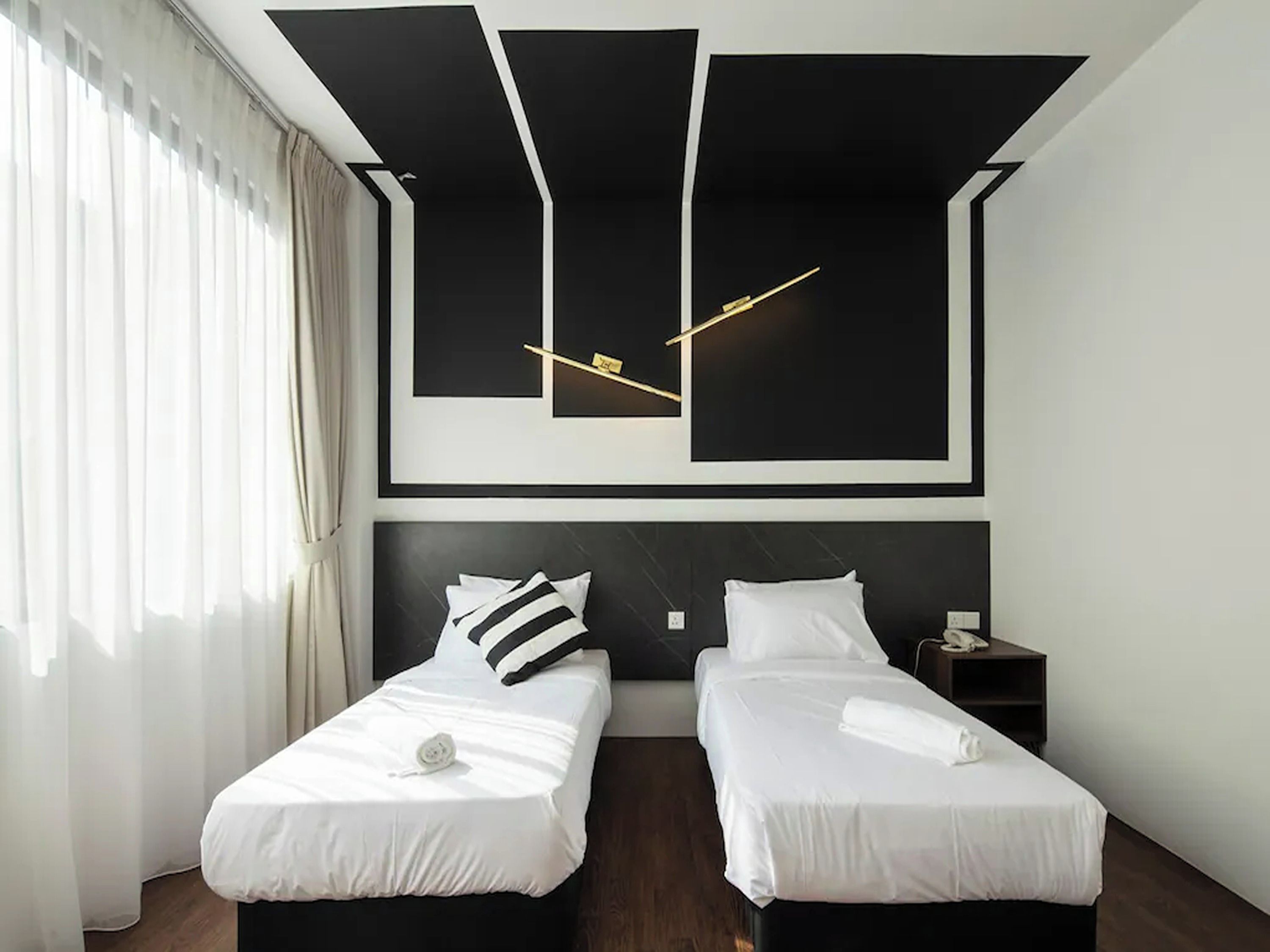 A hotel room with two beds, a modern light fixture, and a large window with curtains.
