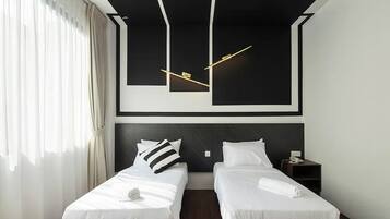 Quarto de hotel com duas camas, luminária moderna e uma grande janela com cortinas.