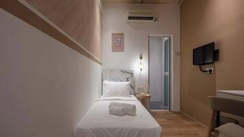 A hotel room with a bed, a desk, a chair, an air conditioning unit, a television, and a door leading to another room.