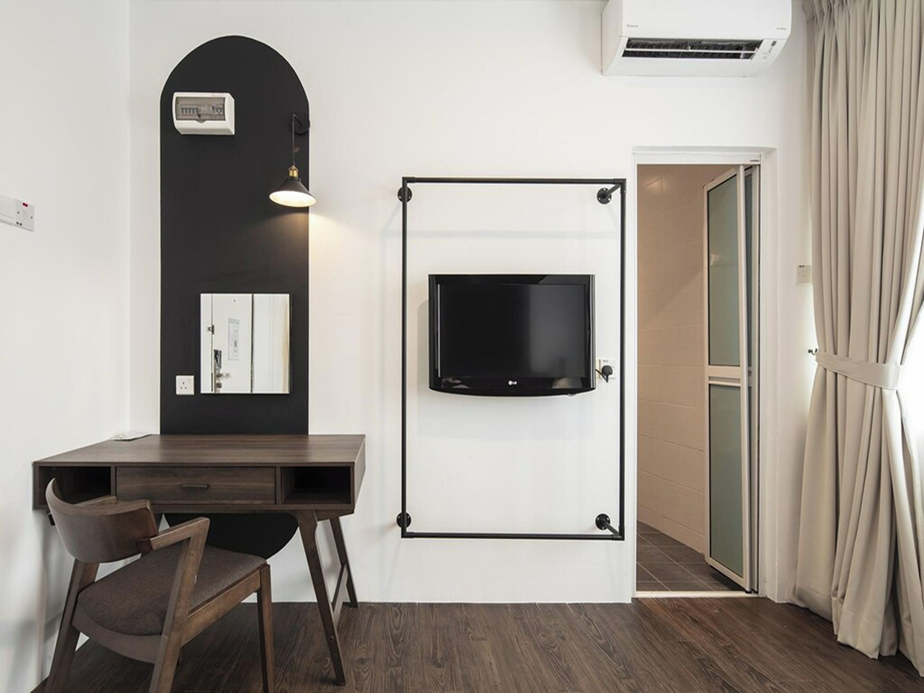 A hotel room with a desk, chair, TV mounted on the wall, and an air conditioning unit.