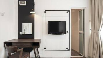 A hotel room with a desk, chair, TV mounted on the wall, and an air conditioning unit.