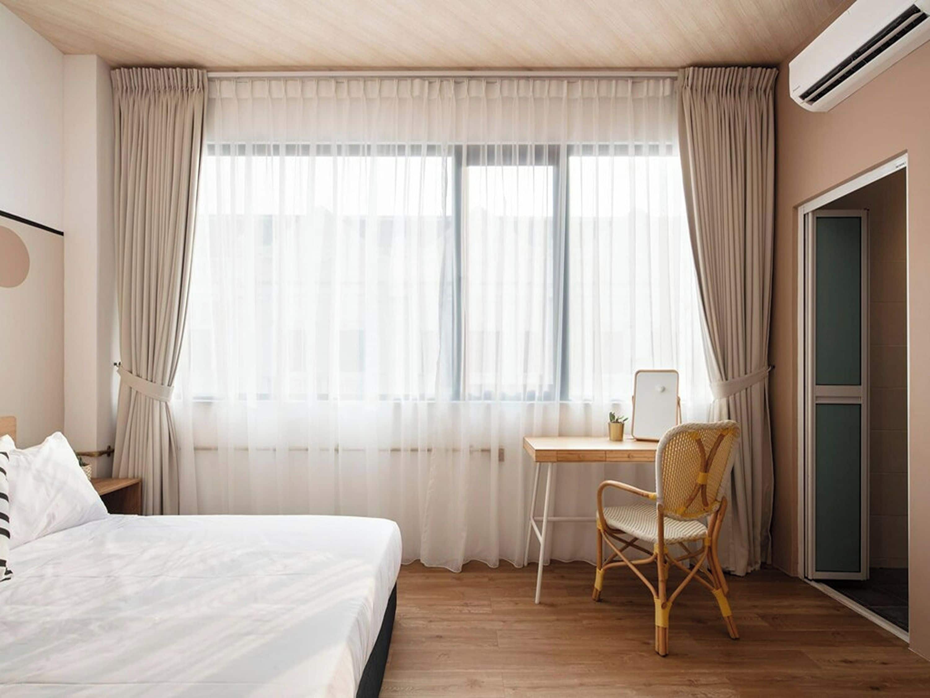 Ein Schlafzimmer mit einem Bett, einem Schreibtisch, einem Stuhl und einem Fenster mit Vorhängen.