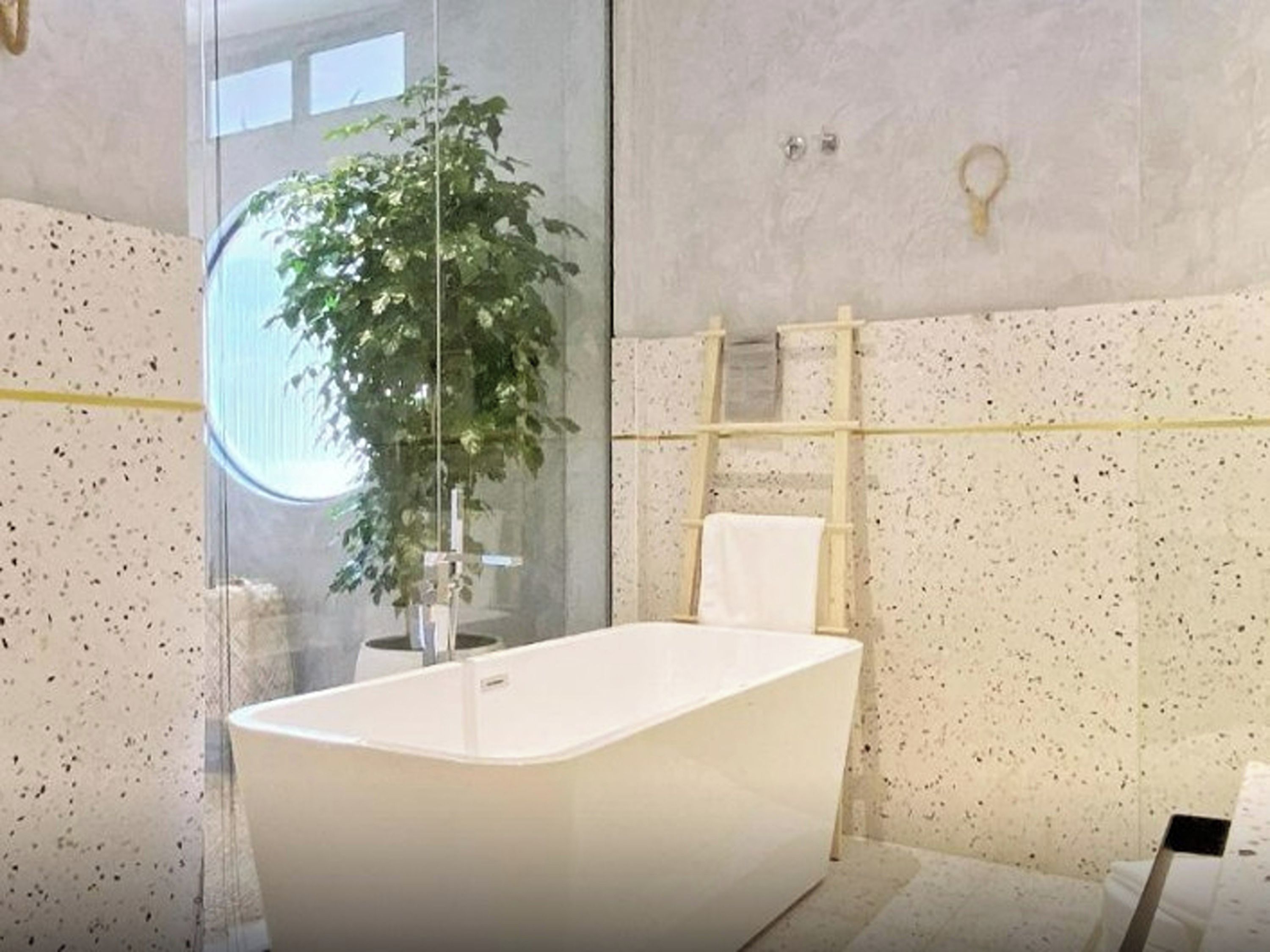 Un baño moderno con una bañera independiente, cabina de ducha con mampara de vidrio y una planta en maceta.