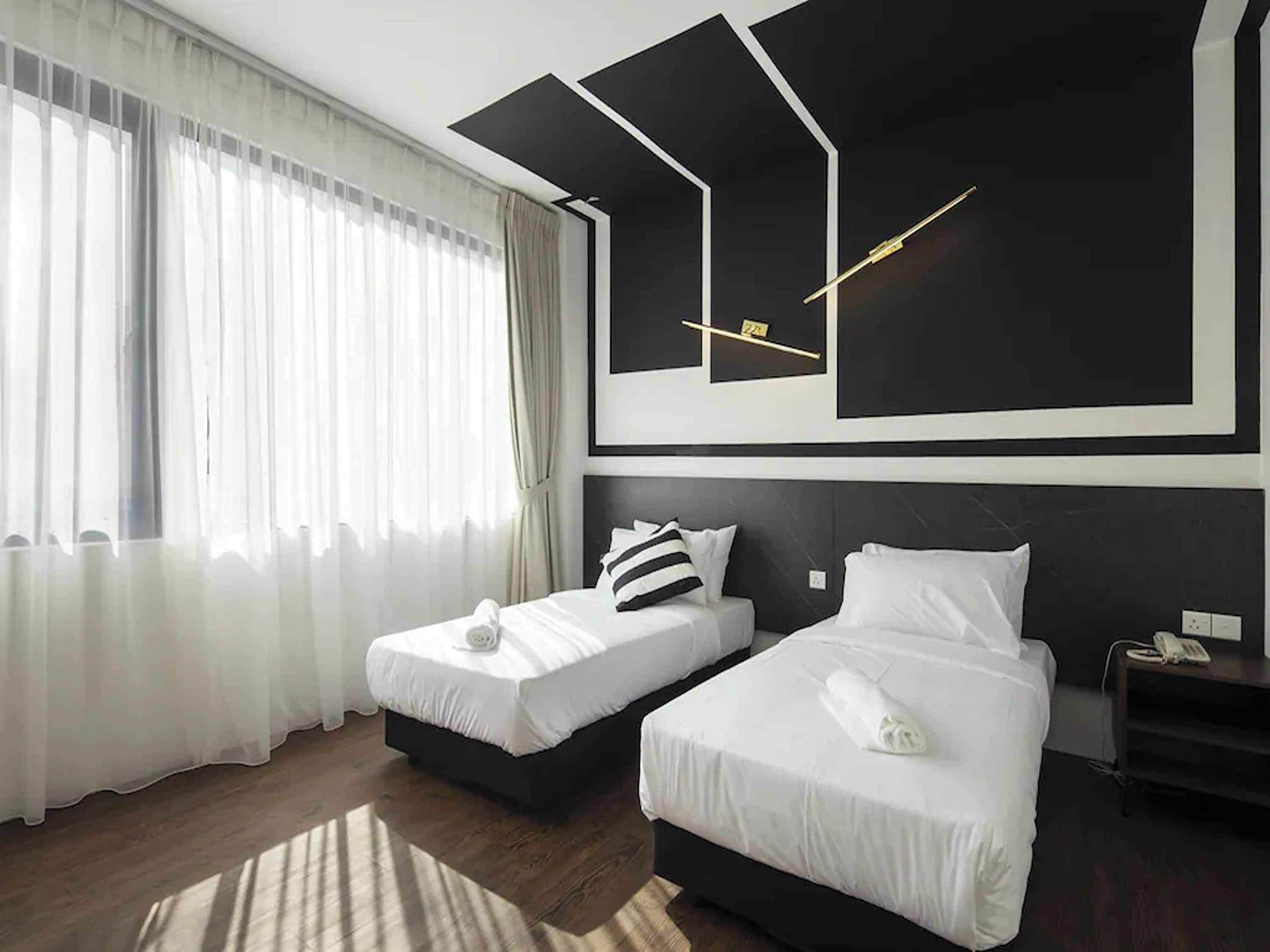 Moderni hotellihuone, jossa on kaksi sänkyä, suuri ikkuna läpikuultavilla verhoilla ja pelkistetty sisustus.
