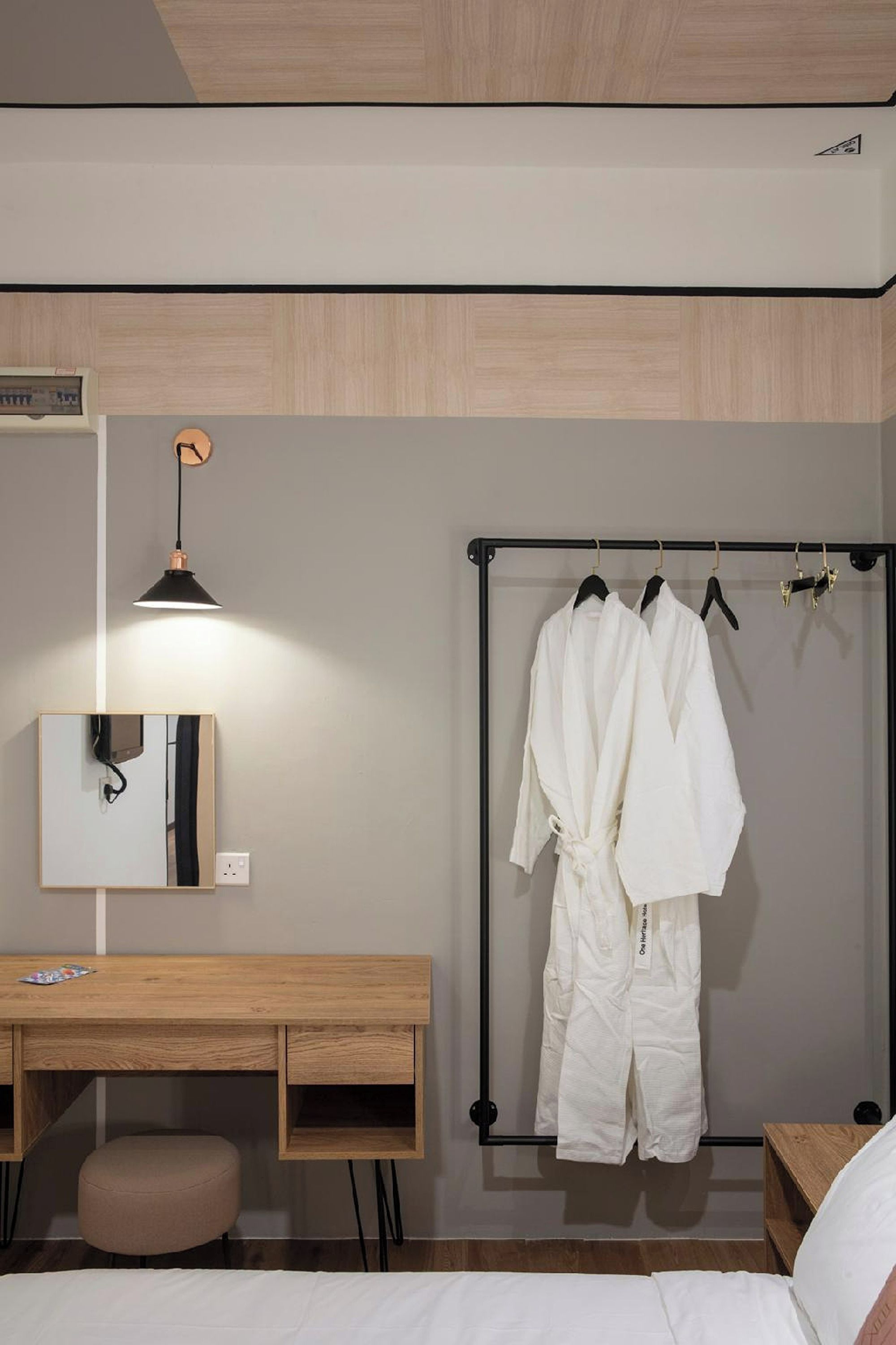 Una habitación de hotel con un escritorio de madera, un perchero, una cama y una mesita de noche.