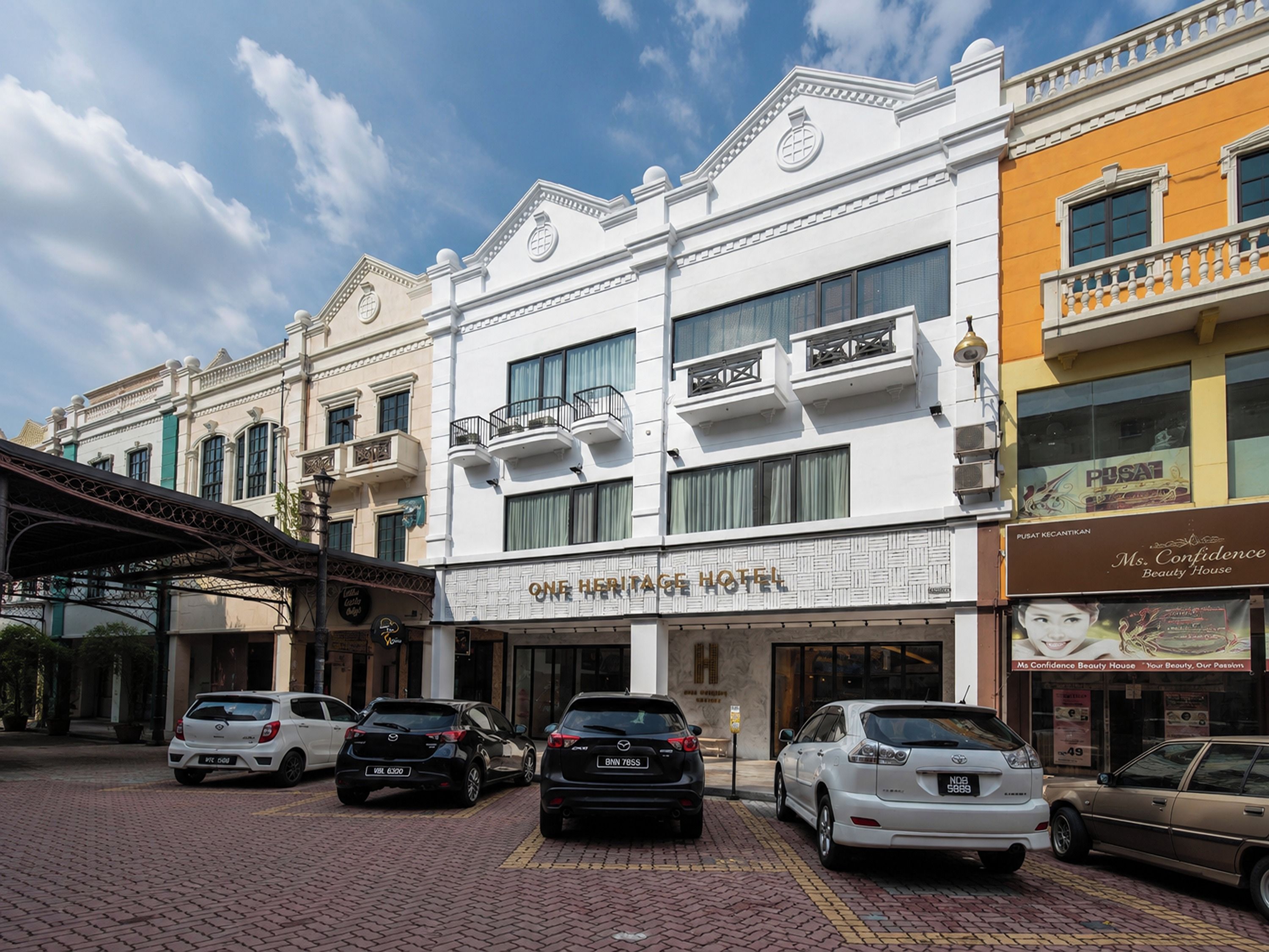 A hotel with a classic facade, multiple balconies, and a parking area with several cars.