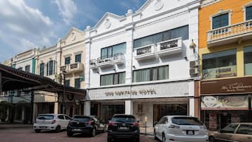 A hotel with a classic facade, multiple balconies, and a parking area with several cars.