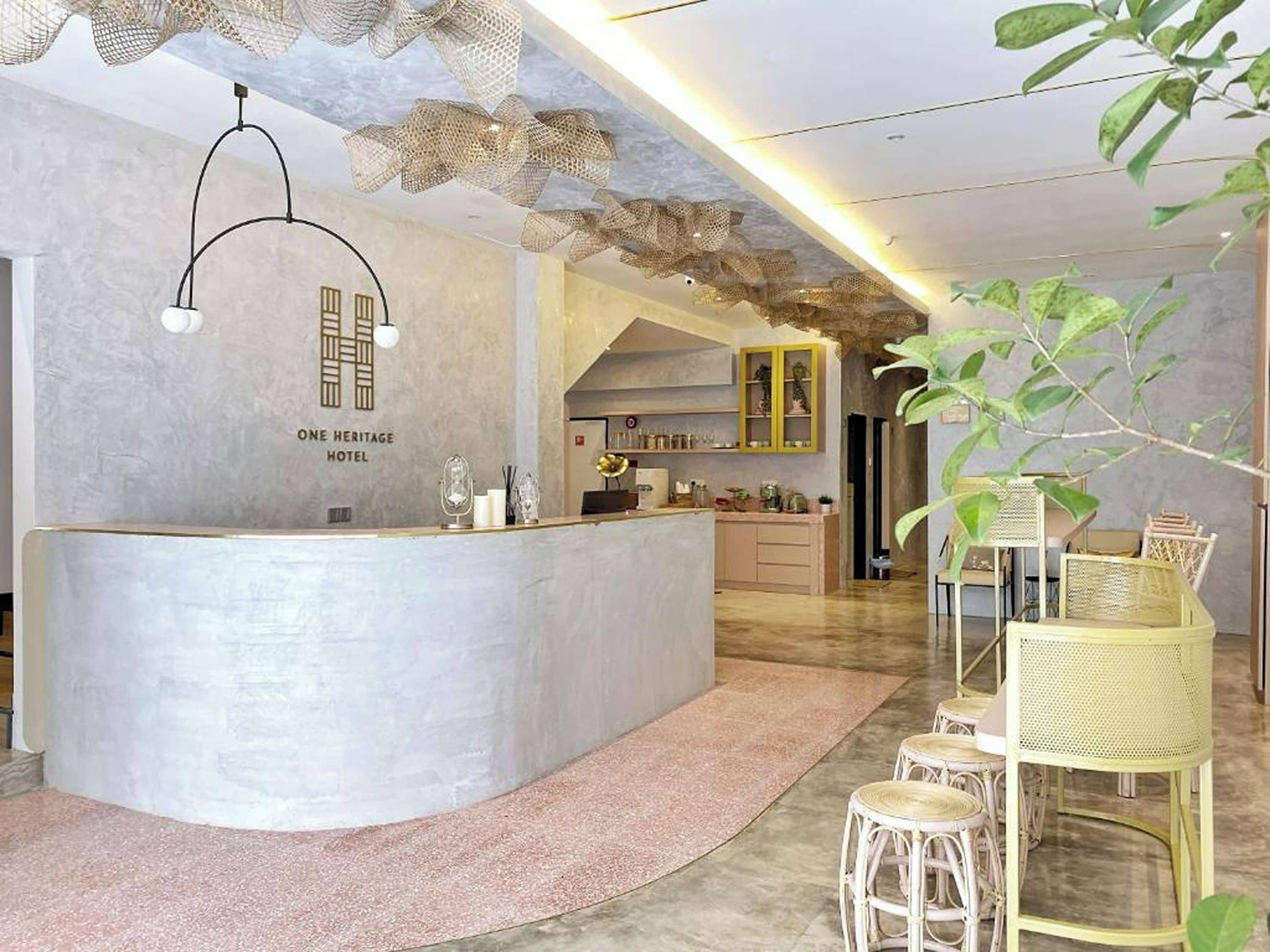 Una zona de recepción con un mostrador curvo, un candelabro y un letrero que dice 'ONE HERITAGE HOTEL'.