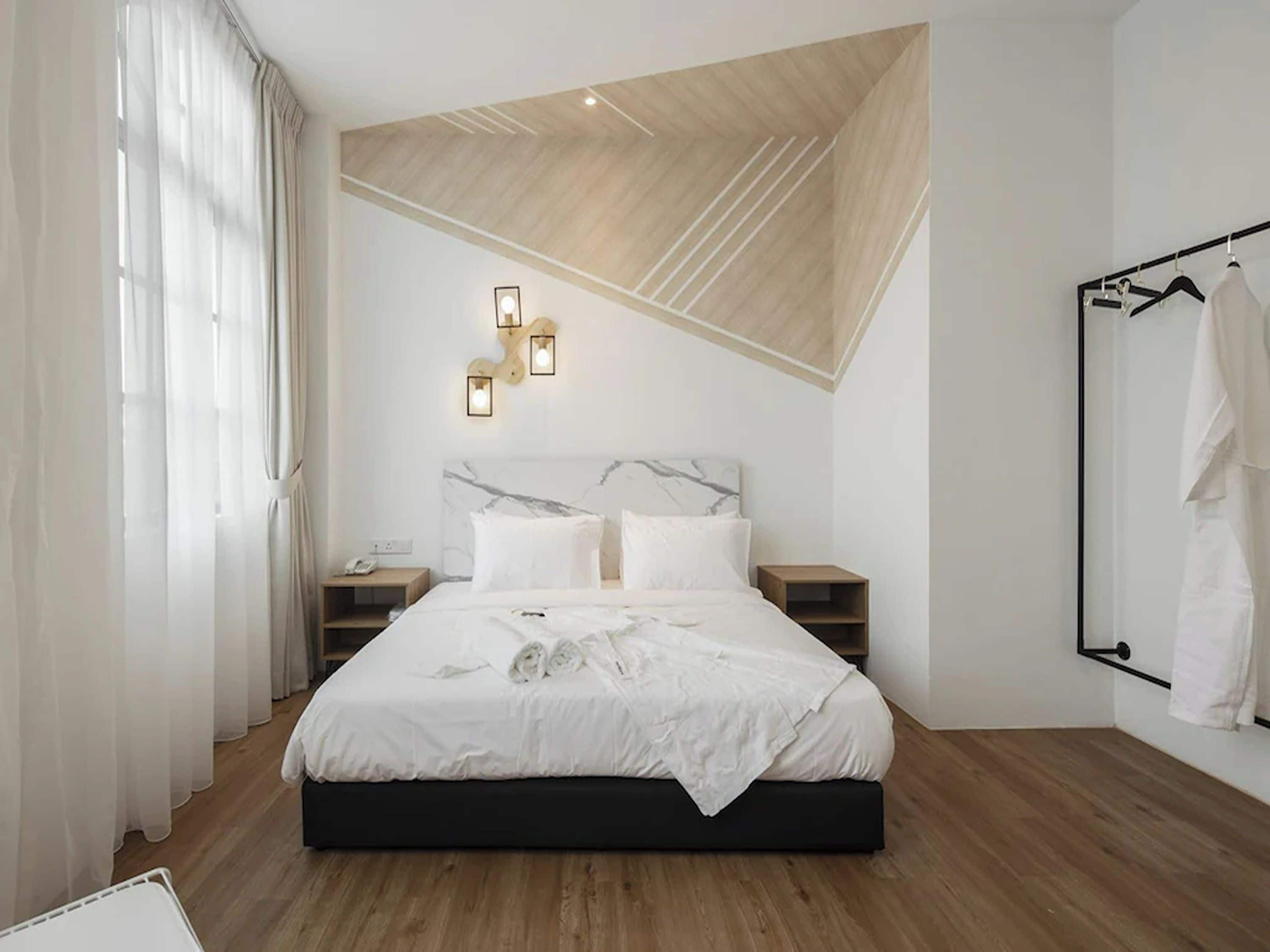 A modern bedroom with a bed, bedside tables, a wall-mounted light fixture, and a clothing rack.