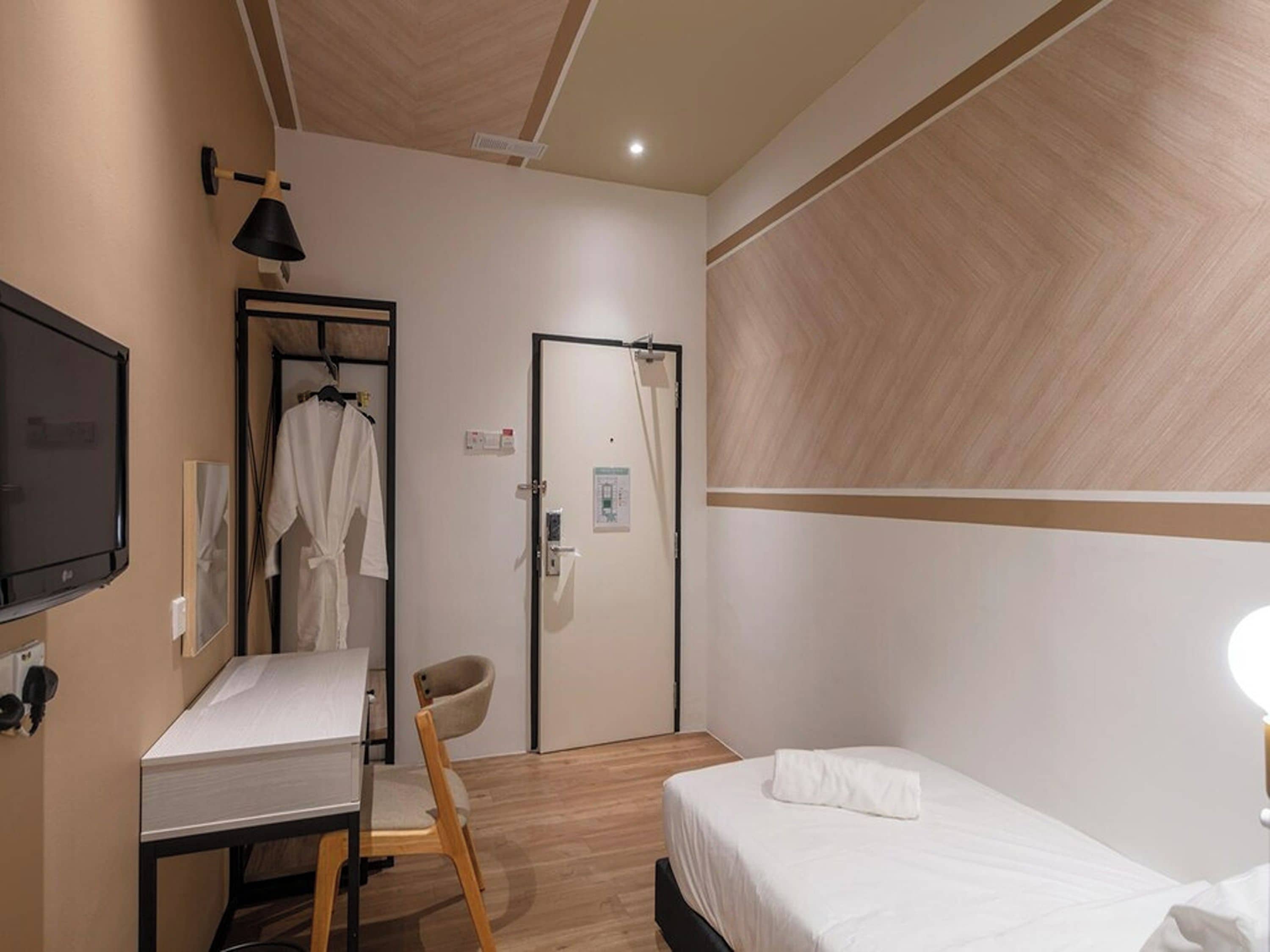 Een hotelkamer met een bed, een bureau, een stoel, een televisie en een deur met een handdoekhouder.
