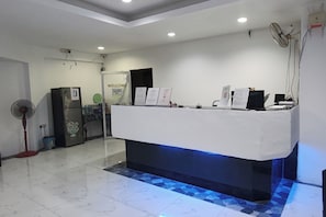 A reception desk with a blue-lit base, a refrigerator, a fan, and a customer entrance sign. - Hotel Medan Kidd (Ipoh)