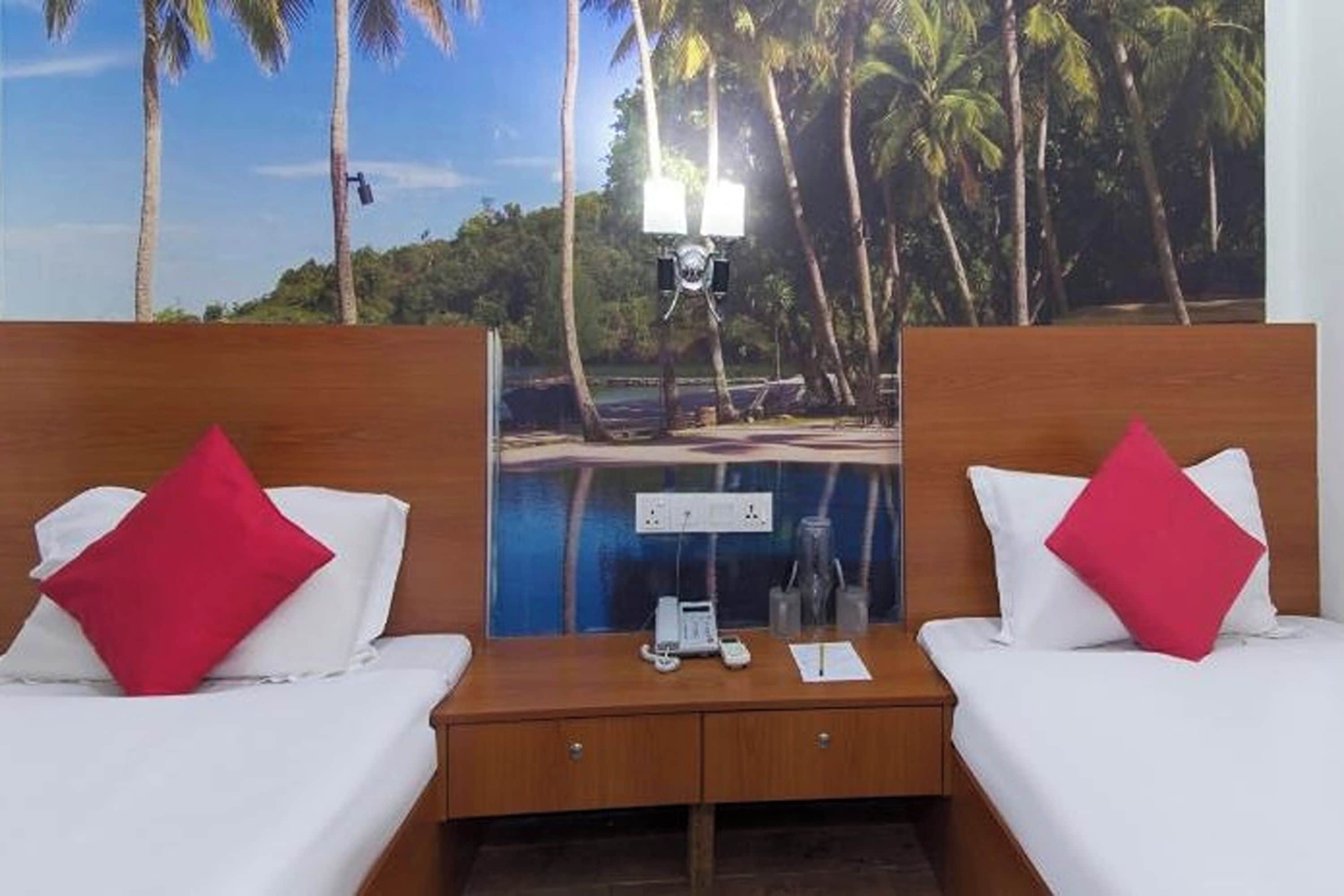 Habitación de hotel con dos camas, cada una con un almohadón rojo, cabeceros de madera y vistas a una piscina a través de una ventana.