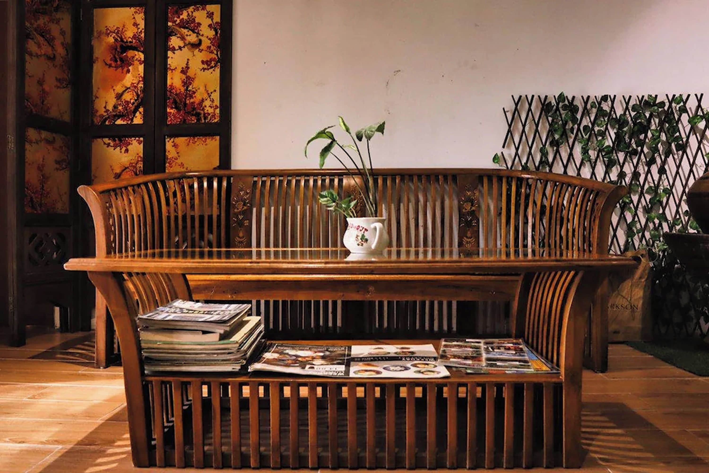 A wooden bench with magazines, a vase with a plant, and a decorative wall with a lattice design.