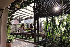 Un espace extérieur aménagé avec des tables et des chaises, entouré de verdure et agrémenté d’une pergola.