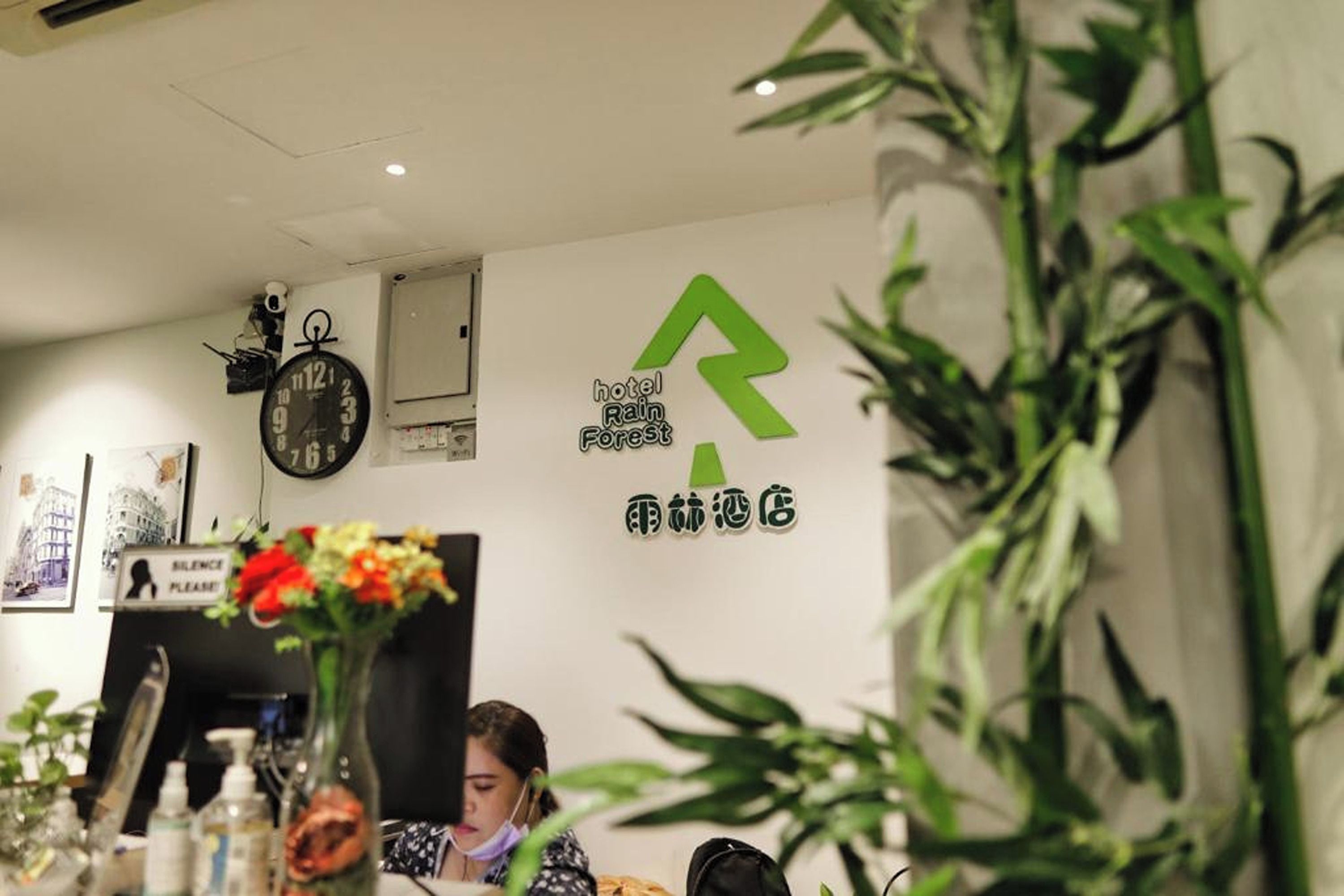 Zona de recepción de un hotel con un reloj, un logotipo verde y un letrero con caracteres chinos.