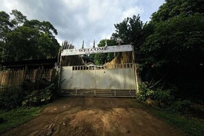 A rustic gate with a 'WELCOME' sign, surrounded by dense greenery.