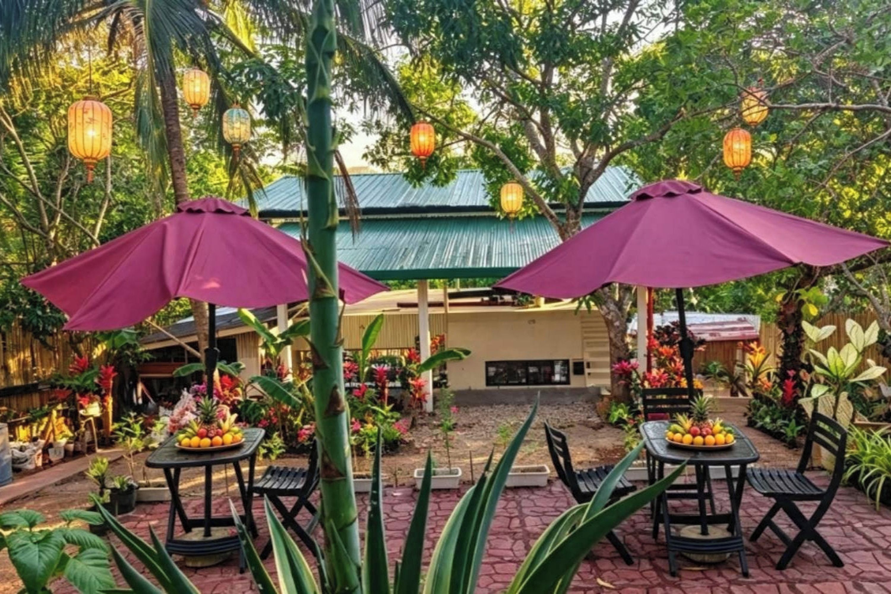 An outdoor seating area with tables and chairs, surrounded by lush greenery and decorative lanterns.