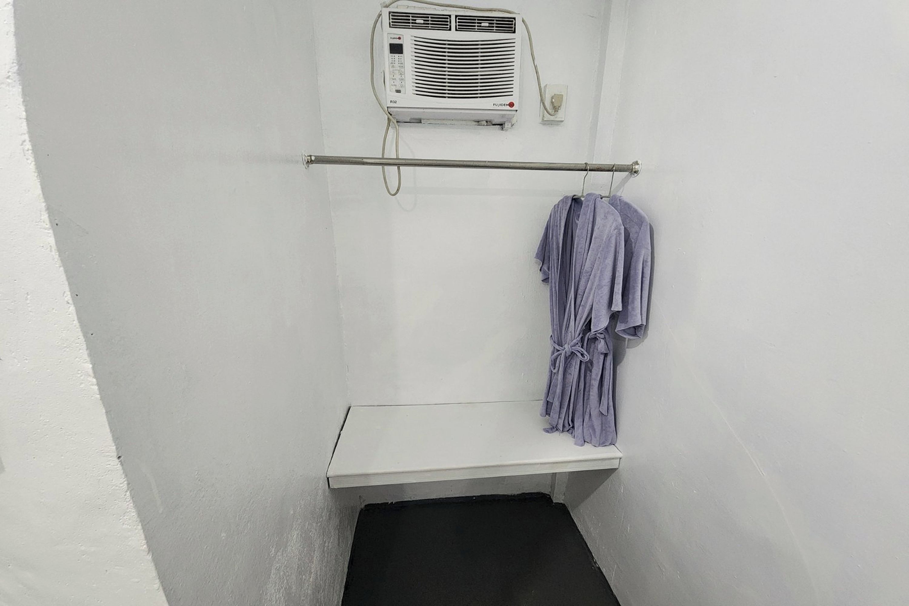 A small, enclosed space with a white wall, a black floor, a white bench, and a towel rack with a towel.