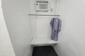 Um espaço pequeno e fechado, com parede branca, chão preto, um banco branco e um porta-toalhas com uma toalha.