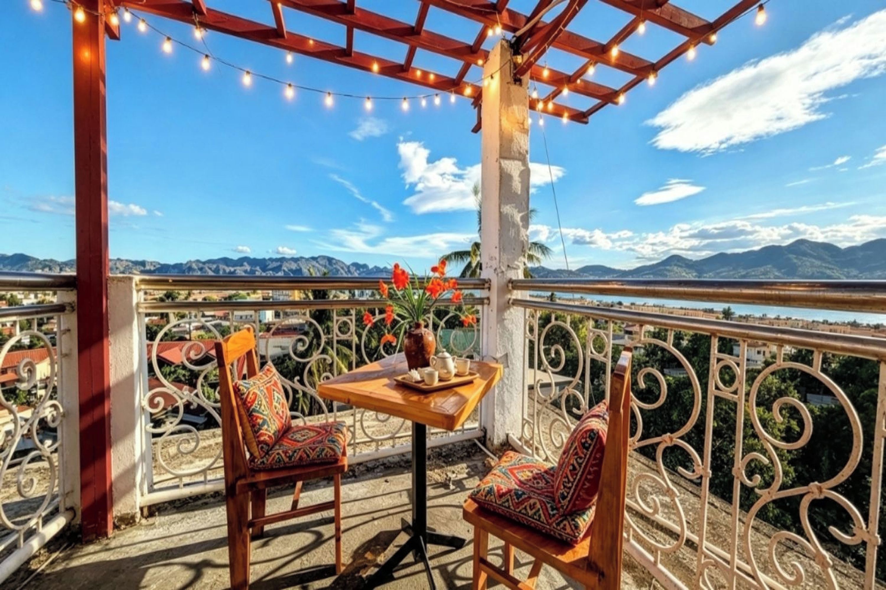 A balcony with a table and chairs, a vase with flowers, and a view of mountains.