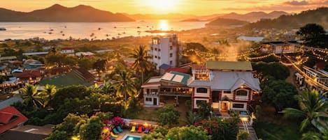 Un resort con piscina, varias edificaciones y vista al atardecer sobre el agua.