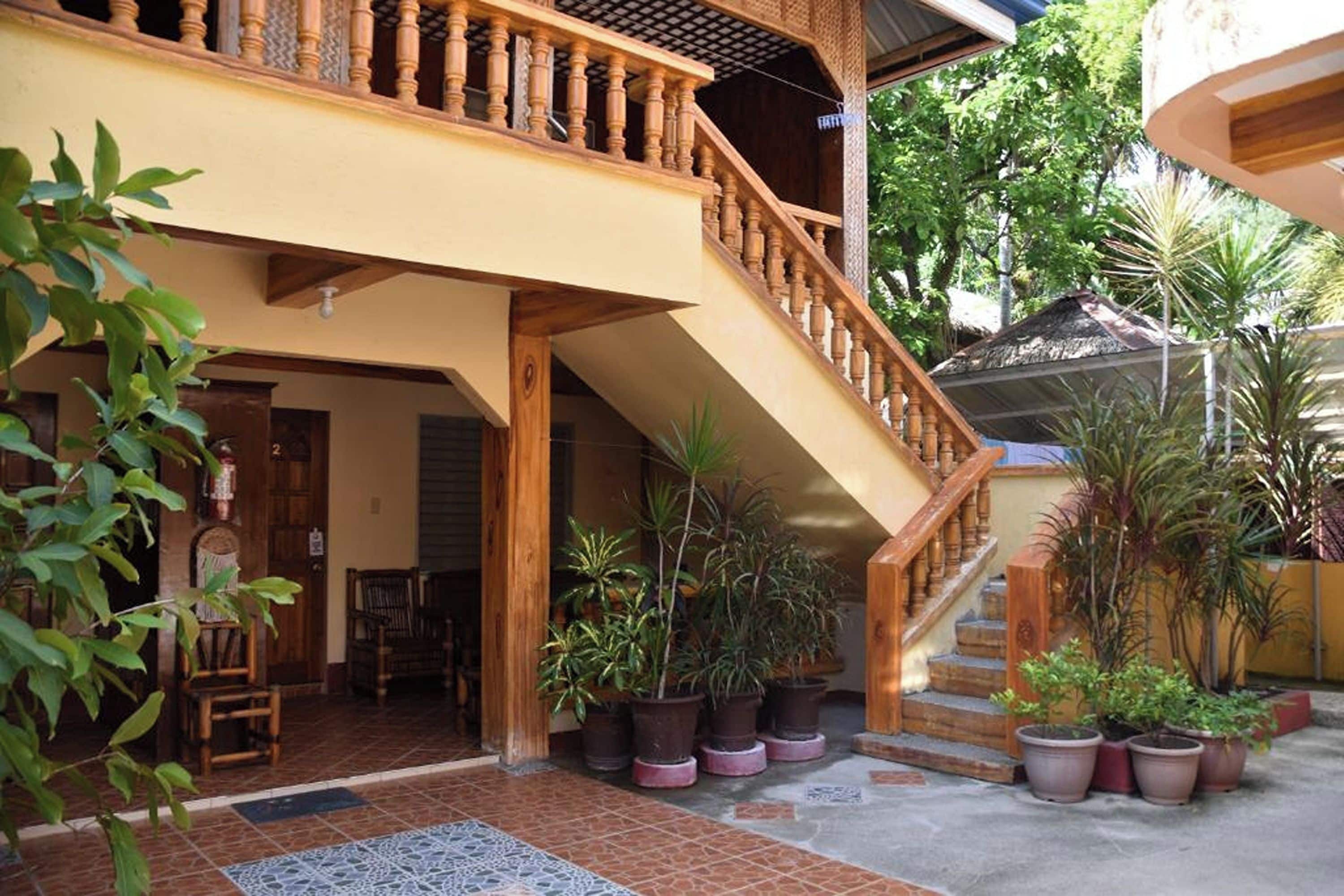 A two-story building with a wooden staircase and multiple potted plants.
