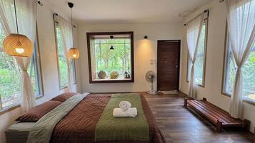 A bedroom with a bed, a bench, a window with a view, and a door.