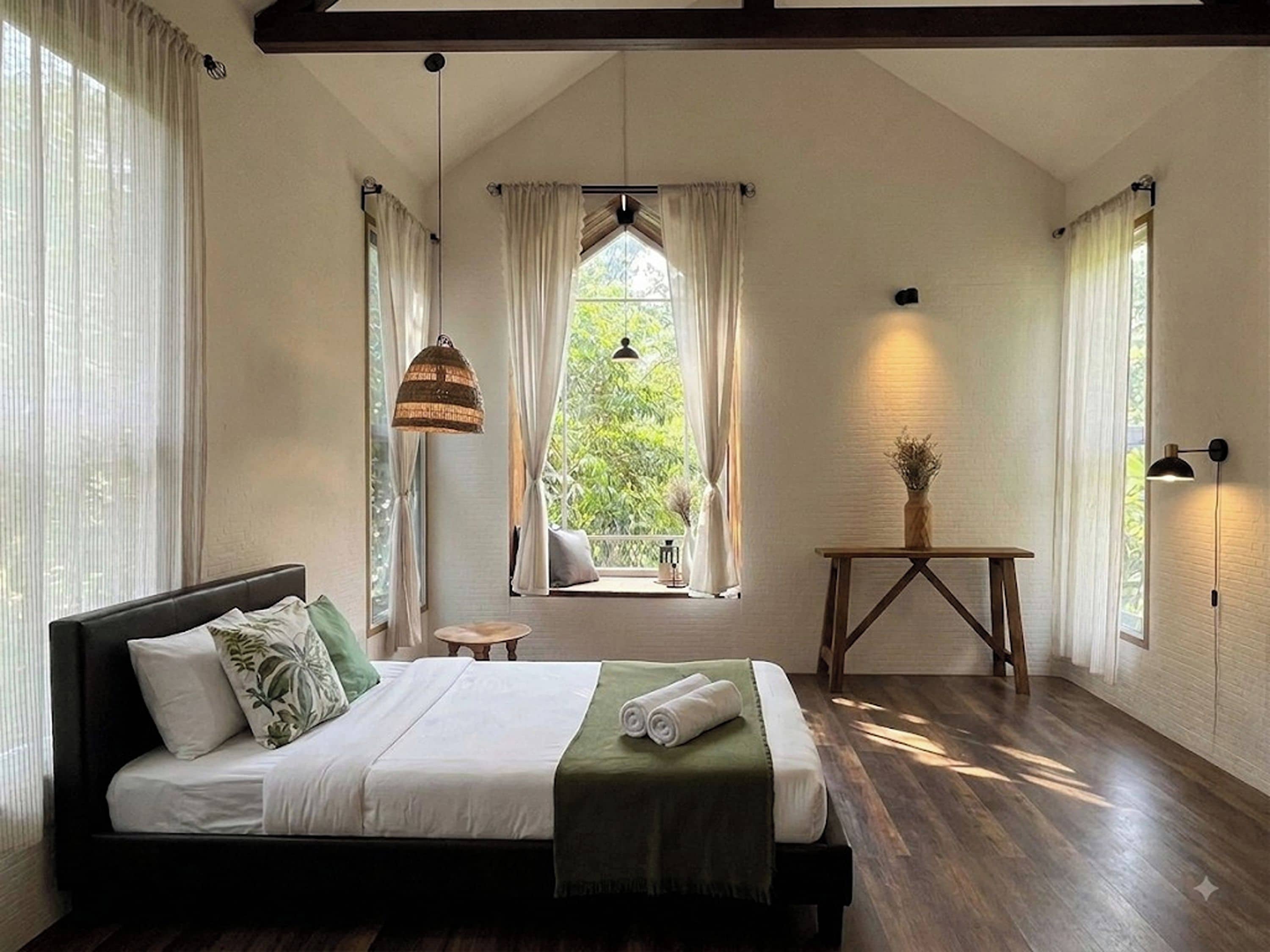 A bedroom with a bed, a window, a table, and a hanging light fixture.