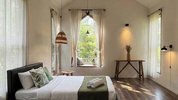 A bedroom with a bed, a window, a table, and a hanging light fixture.