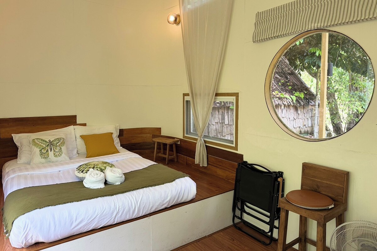A bedroom with a bed, a window, a chair, and a fan.