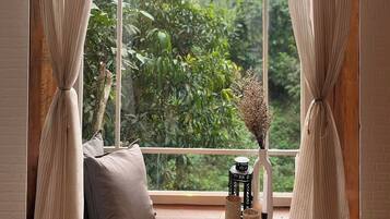 A room with a large window, a hanging lamp, a cushion, and a small table with decorative items.