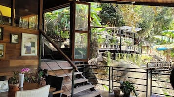 Una escalera de madera lleva a un balcón con vistas a un jardín y un pequeño espacio exterior con mesa y sillas.