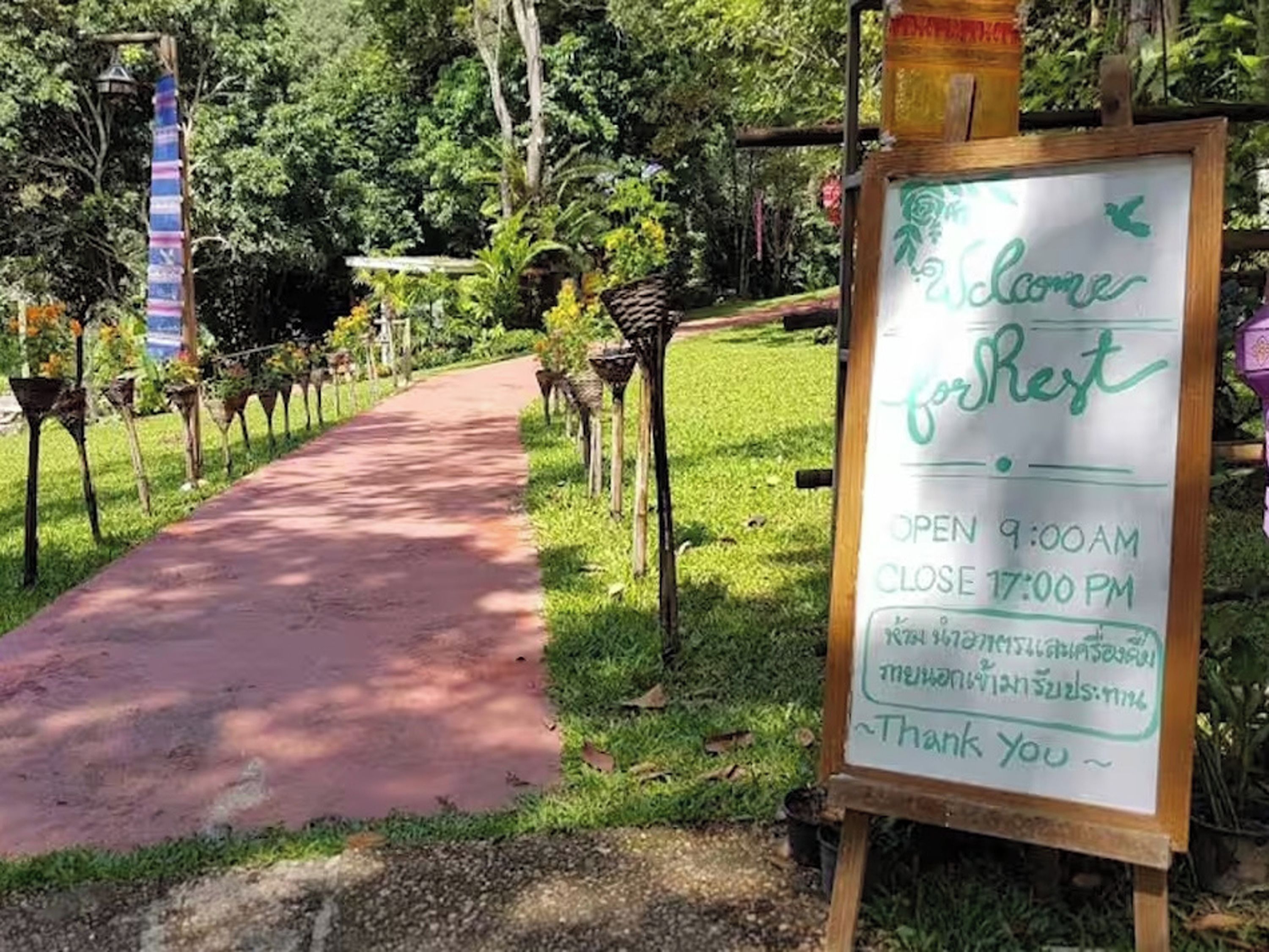 A sign welcoming visitors to a park with a pathway, surrounded by greenery and decorative elements.