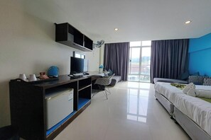 Habitación de hotel moderna con una televisión de pantalla plana, un escritorio con ordenador, un sofá y un ventanal con cortinas.