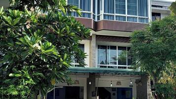 Un edificio moderno con entrada en esquina, un área de estar exterior cubierta con mesas y sillas, y una motocicleta estacionada afuera.